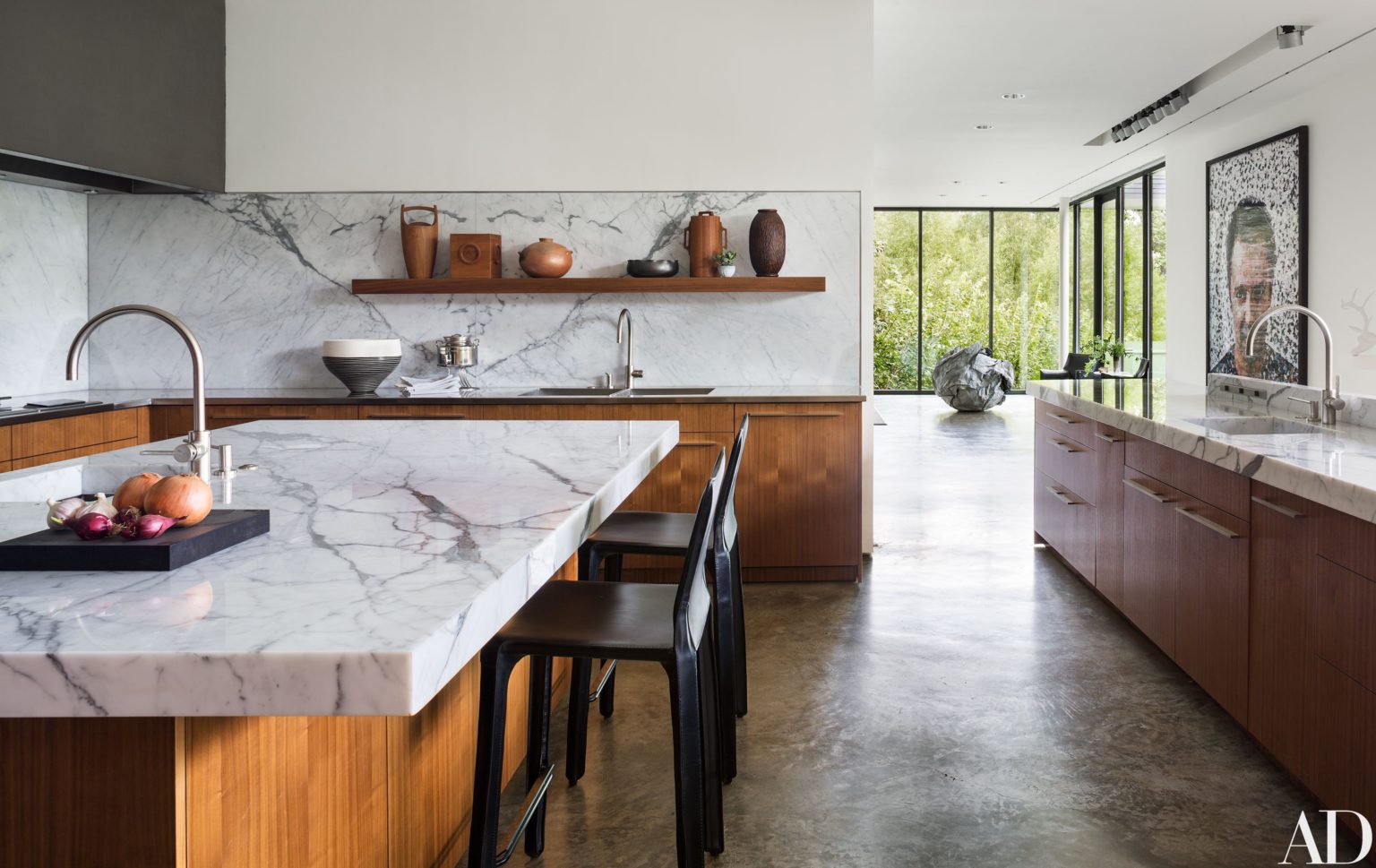 A modern kitchen featuring elegant marble countertops with natural veining, complemented by wooden cabinetry and stainless steel fixtures. The large island serves as a central element, enhancing the luxurious and spacious feel of the kitchen.